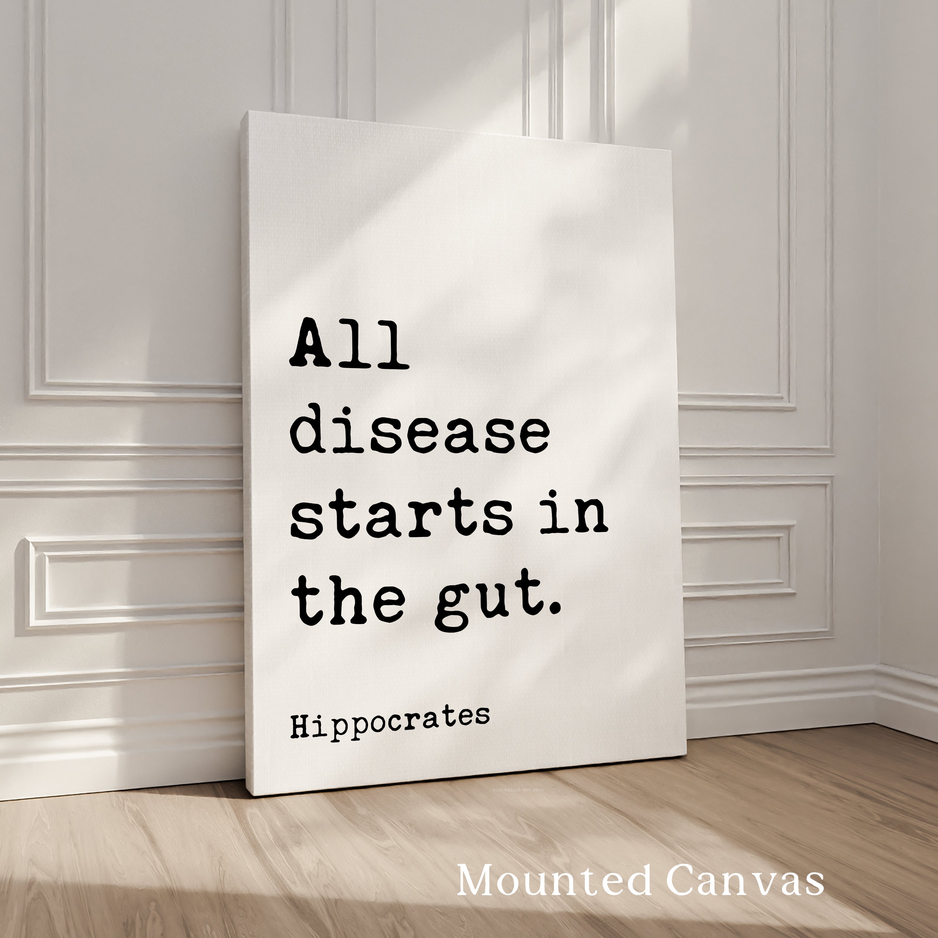 A white canvas with black text that reads "All disease starts in the gut. Hippocrates" against a white wall background.