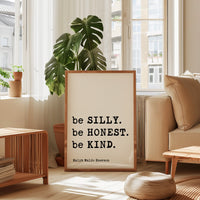 a framed quote by Ralph Waldo Emerson, "be SILLY. be Honest. be KIND.", placed in a living room setting with a potted plant and a window.