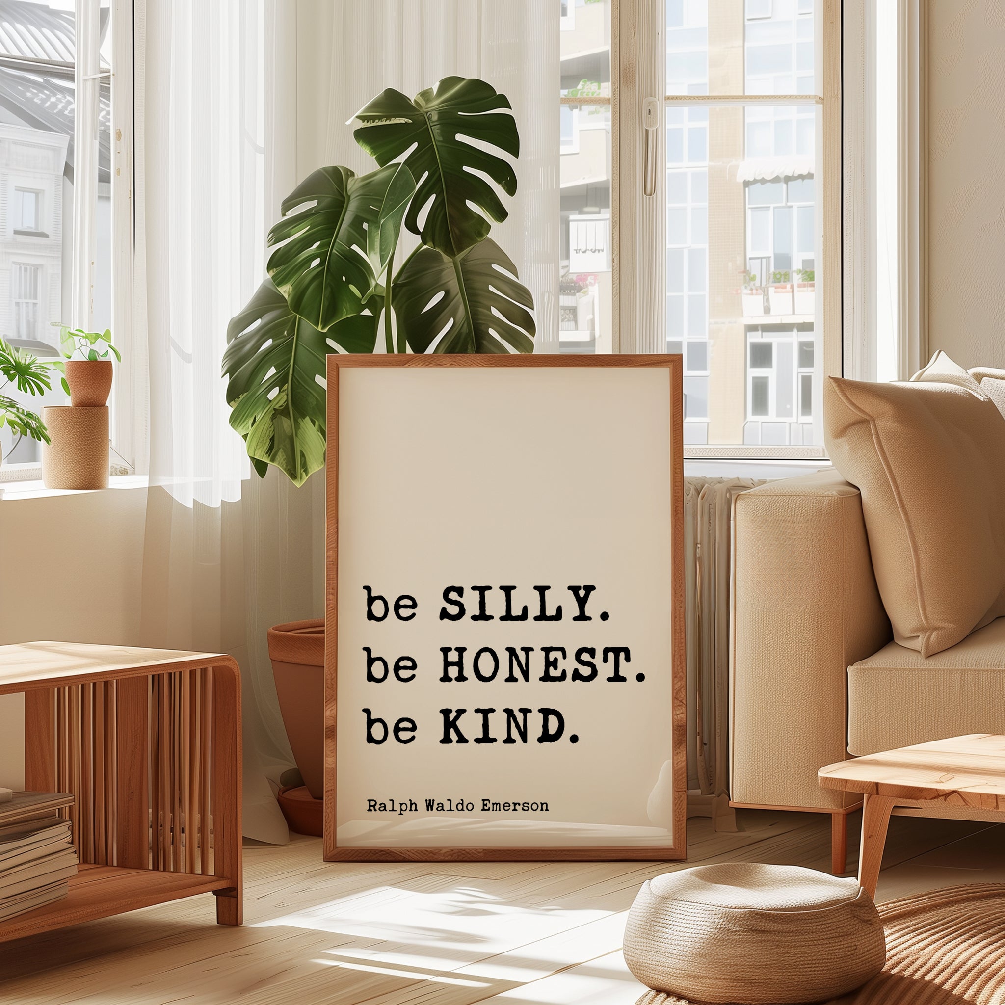 a framed quote by Ralph Waldo Emerson, "be SILLY. be Honest. be KIND.", placed in a living room setting with a potted plant and a window.