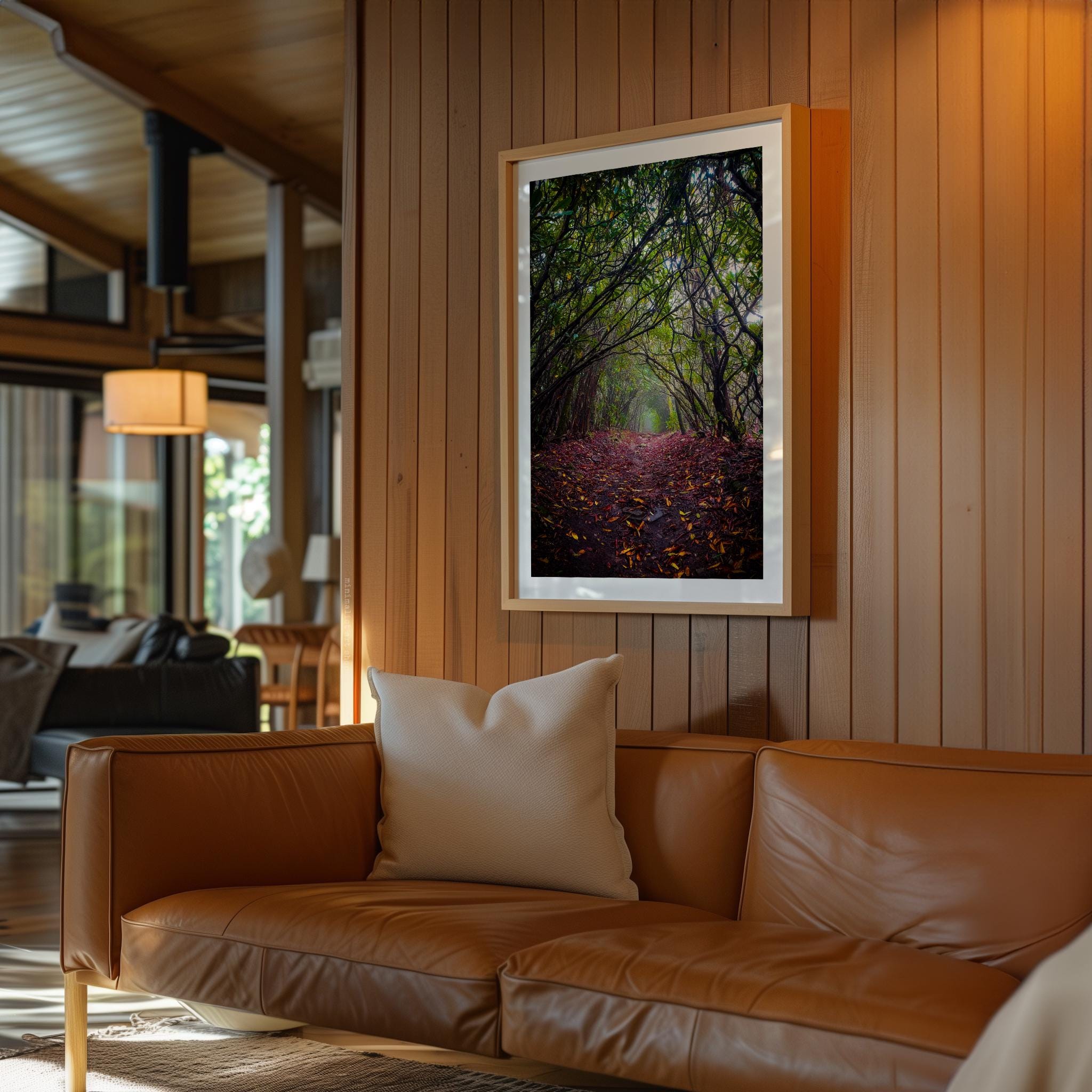 a cozy living room with a brown leather sofa, a framed photograph of a forest path, and a wooden wall.