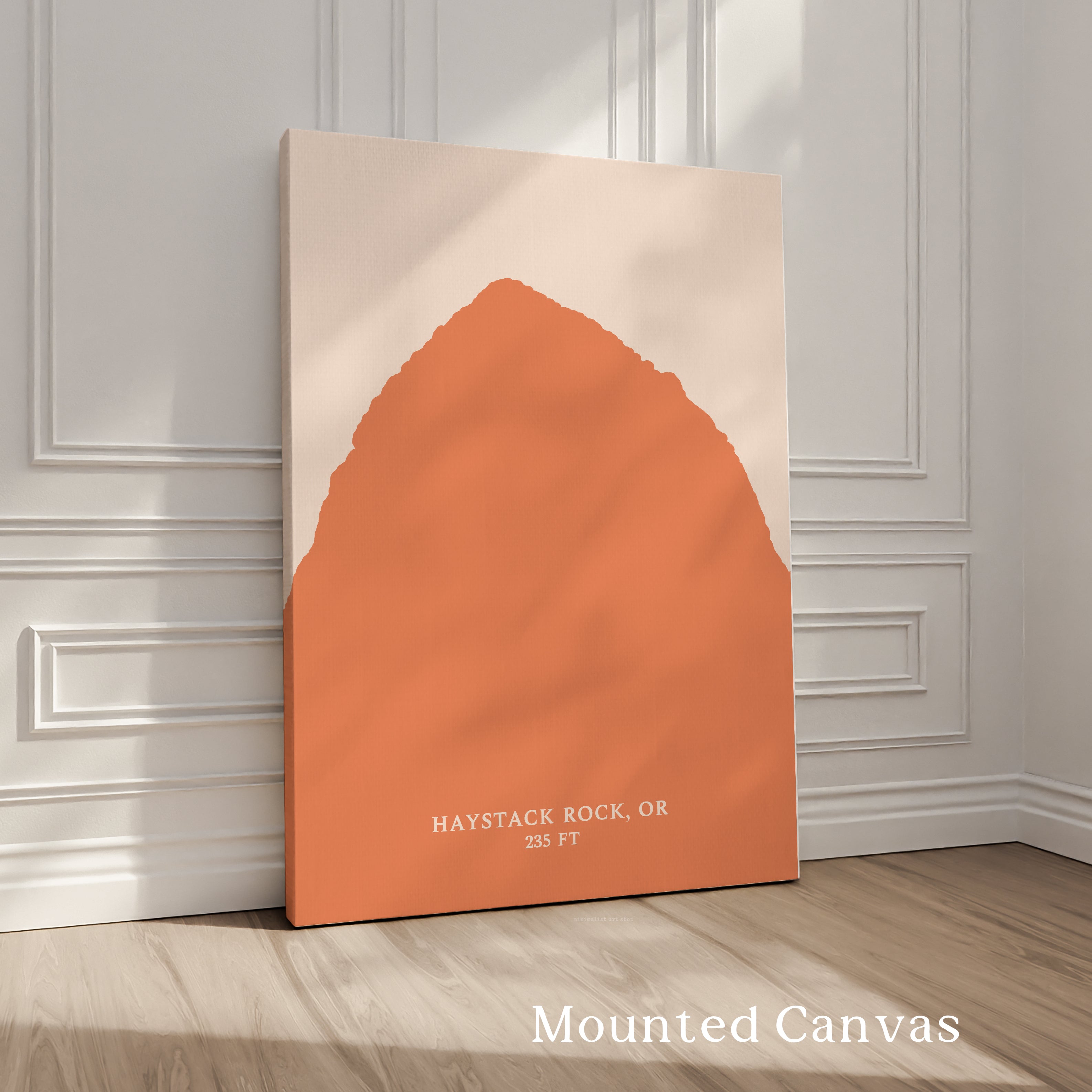 a large canvas print of a mountain range, with a prominent orange shape in the center. The text "HAYSTACK ROCK, OR" is visible, indicating the location or subject of the artwork.