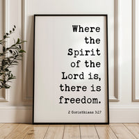 A framed poster with the text "Where the Spirit of the Lord is, there is freedom." and the Bible verse "2 Corinthians 3:17" is displayed on a wooden floor against a white wall.