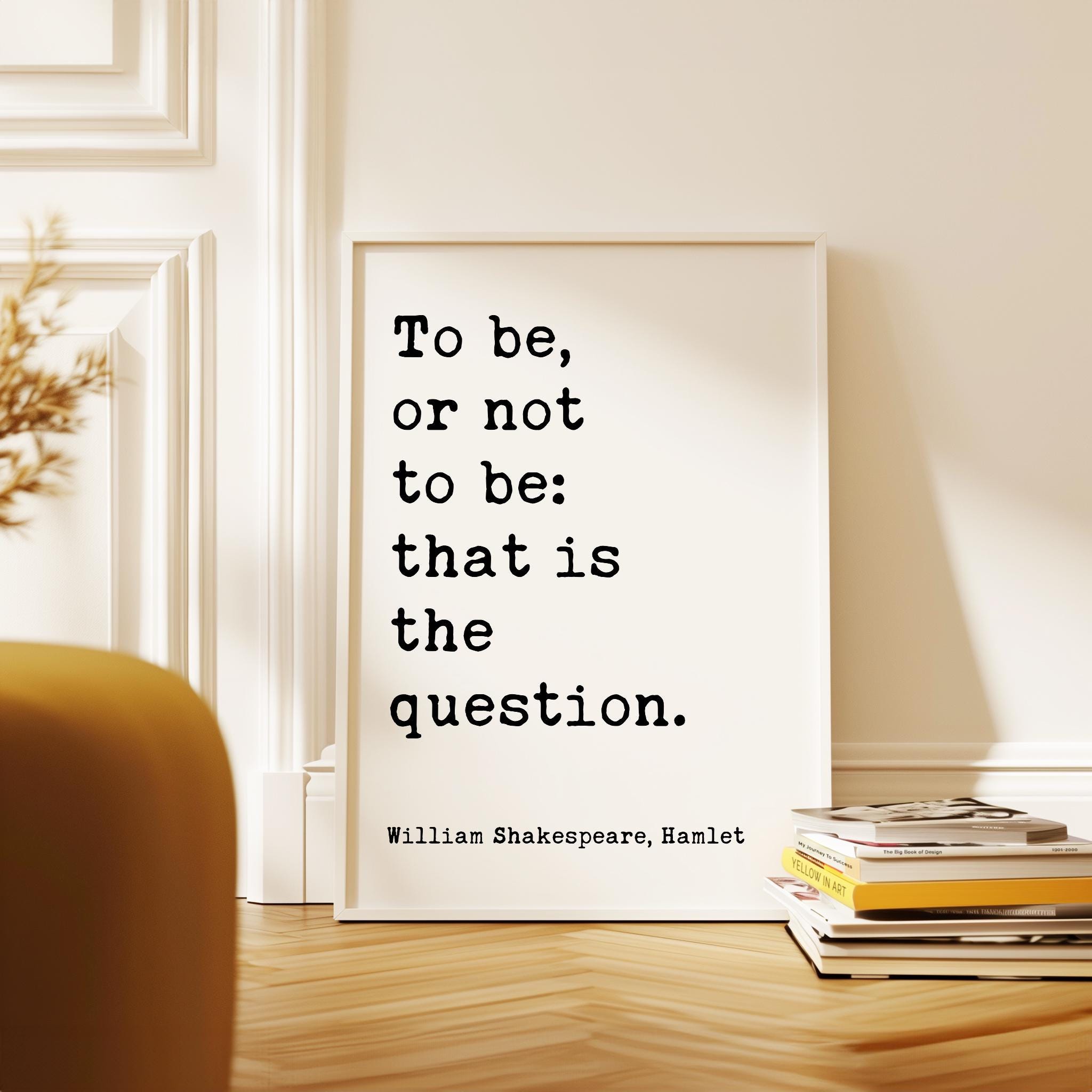 a quote by William Shakespeare, "To be, or not to be: that is the question." The quote is displayed on a white poster, which is propped up against a white wall. In the foreground, there is a stack of books and a plant.