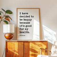 a framed quote by Voltaire, "I have decided to be happy because it's good for my health," placed on a wooden cabinet or dresser.