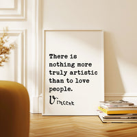 a quote by Vincent Van Gogh, which reads "There is nothing more truly artistic than to love people." The quote is displayed on a white poster, which is leaning against a white wall. In the foreground, there is a stack of books and a plant.