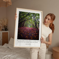 A woman holds up a framed photograph of a forest path with fallen leaves, accompanied by a quote about nature and the value of every walk.