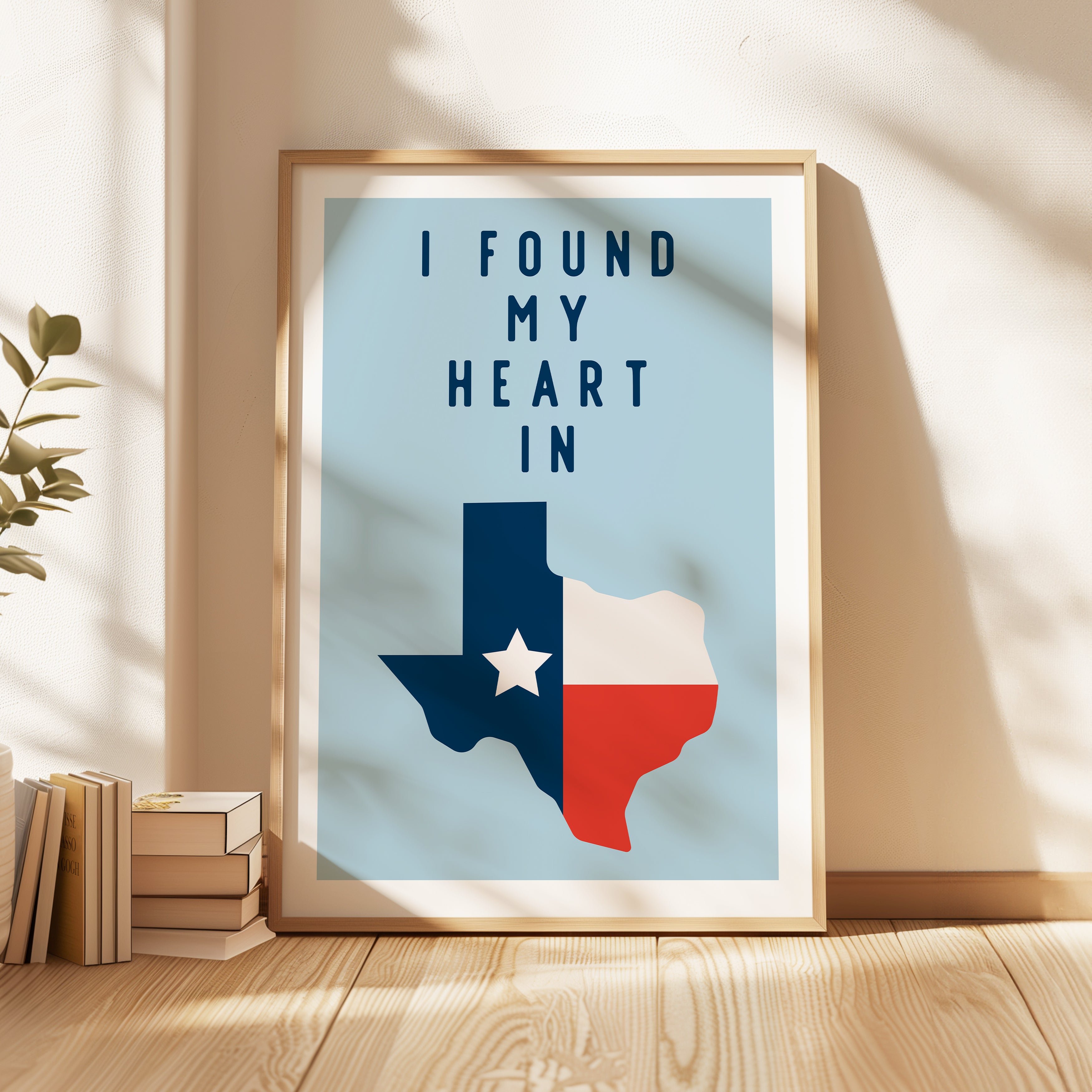 A framed poster with the text "I FOUND MY HEART IN" and a graphic of the state of Texas, with a stack of books and a plant to the side.