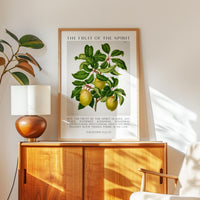 May include: A framed botanical print titled "The Fruit of the Spirit." The artwork features a detailed illustration of a fruit-bearing branch with green leaves and yellow-green fruit. Text from Galatians 5:22-23 is below the image.