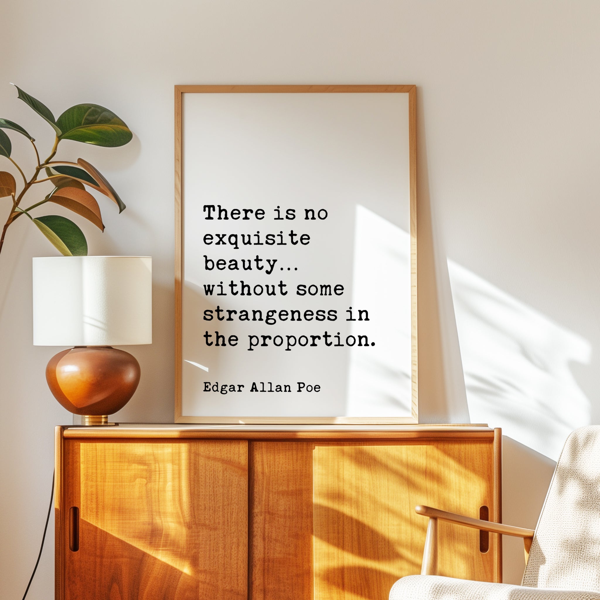 a framed quote by Edgar Allan Poe, "There is no exquisite beauty... without some strangeness in the proportion." The quote is displayed on a wooden cabinet or dresser, with a lamp and a plant nearby.