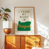 a framed poster with the text "I FOUND MY HEART IN OREGON" displayed on a wooden cabinet.