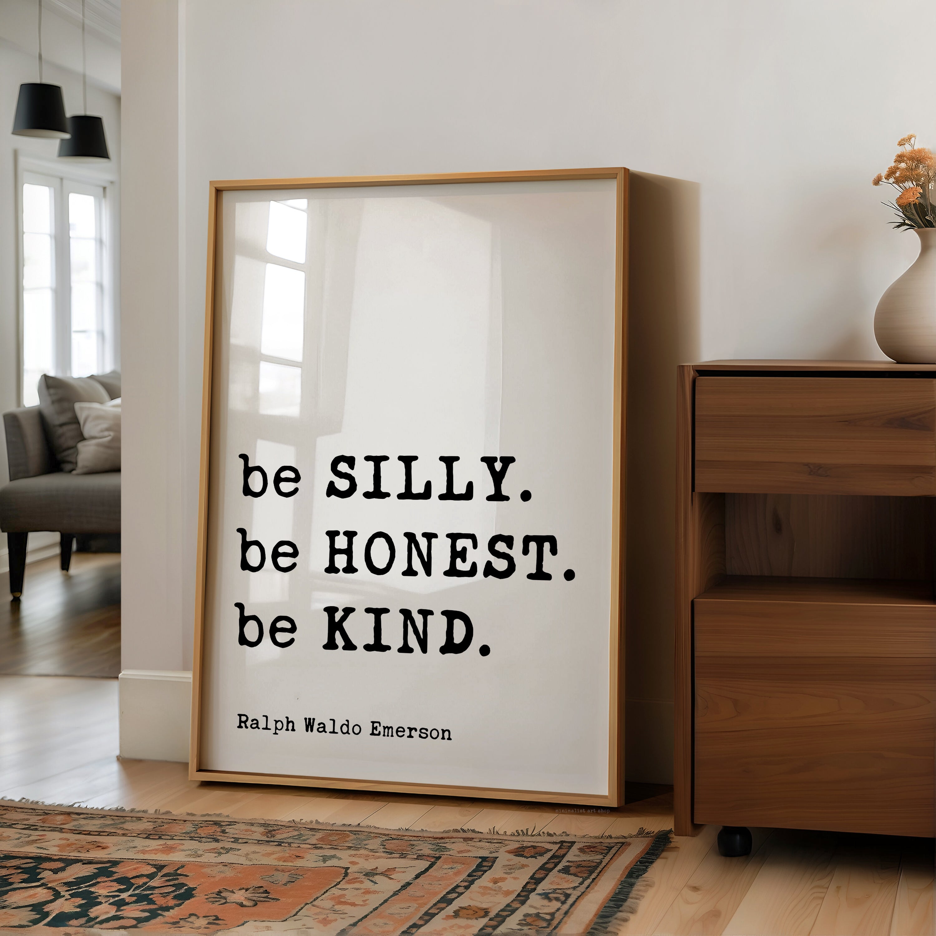A framed quote by Ralph Waldo Emerson, "be SILLY, be HONEST, be KIND," is displayed on a wall in a living room.
