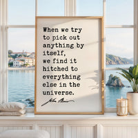 a framed quote by John Muir, which reads: "When we try to pick out anything by itself, we find it hitched to everything else in the universe." The quote is displayed in a white frame, and the background shows a scenic view of a body of water and a distant island.