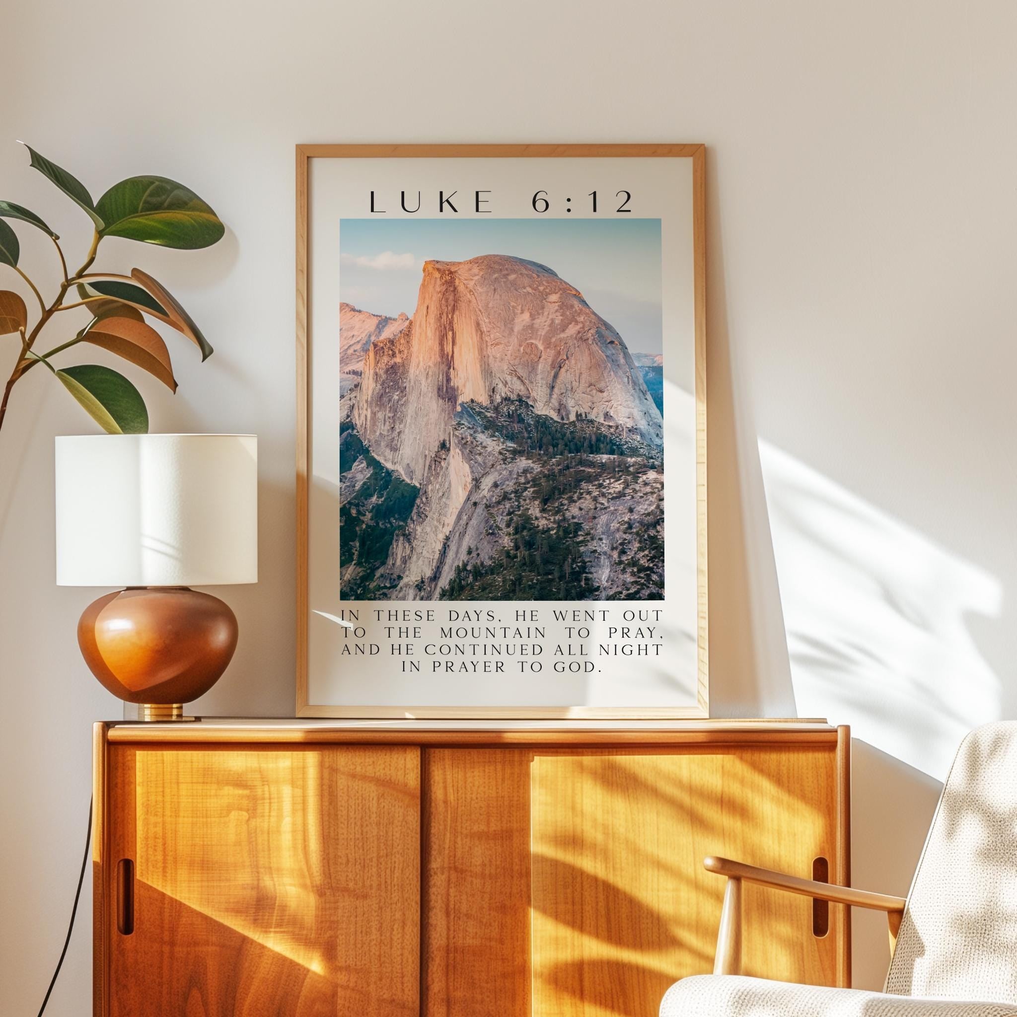 A framed poster of a mountain landscape hangs on a wall, accompanied by a lamp and a plant in a wooden cabinet.