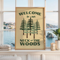 May include: A rectangular wall art print in a light wood frame featuring a cream background with dark green text that reads WELCOME to our NECK of THE WOODS. The design includes a central illustration of five stylized pine trees in green.