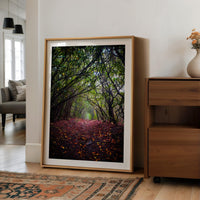 a large framed photograph of a forest path with fallen leaves, placed on a wooden floor next to a wooden dresser.