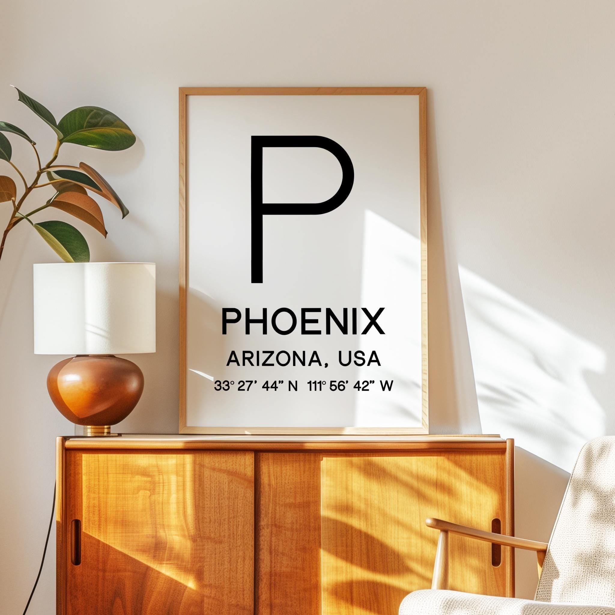 a framed poster with the text "PHOENIX, ARIZONA, USA" and a coordinate system, along with a lamp and a plant on a wooden cabinet.
