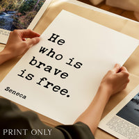 A person's hands holding a piece of paper with the text "He who is brave is free." printed on it.