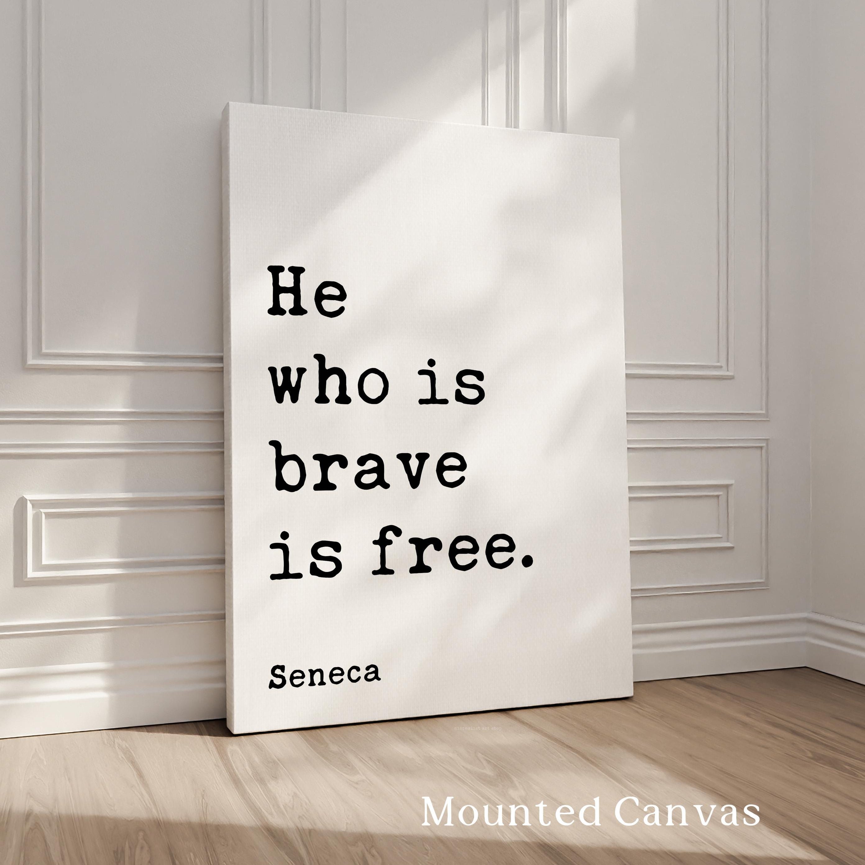 A white canvas with the quote "He who is brave is free" by Seneca, standing on a wooden floor against a white wall.