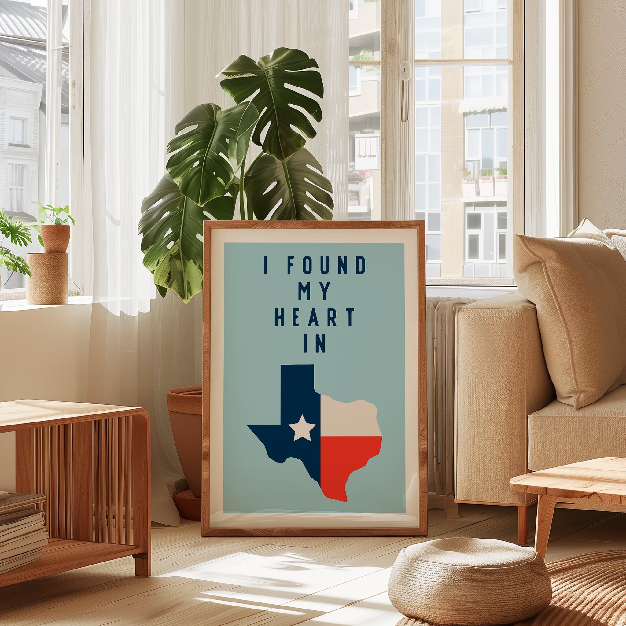 a framed poster with a Texas state map and the text "I FOUND MY HEART IN" displayed in a living room setting with a window, potted plants, and a couch.
