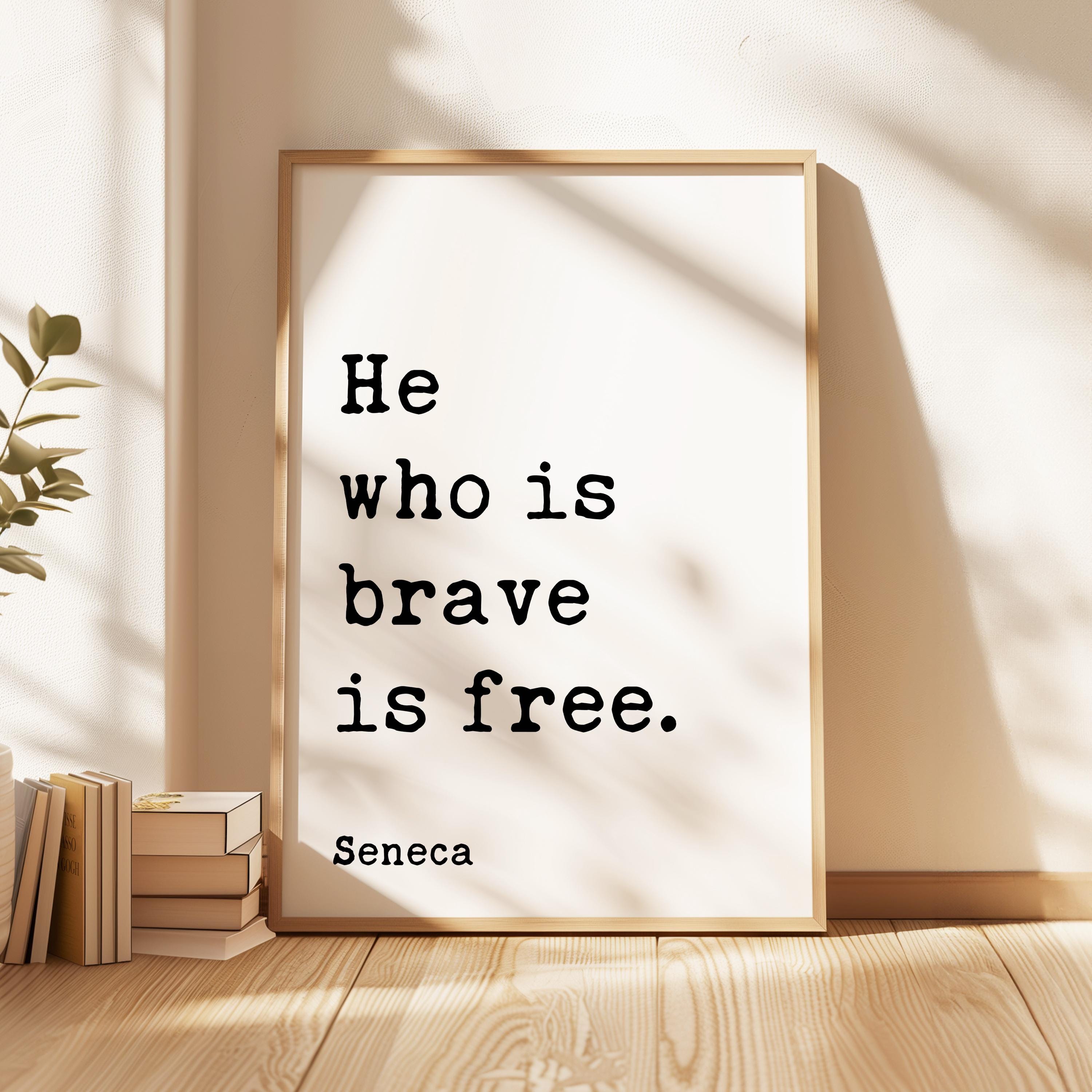 a framed quote by Seneca, "He who is brave is free", placed on a wooden floor next to a stack of books.