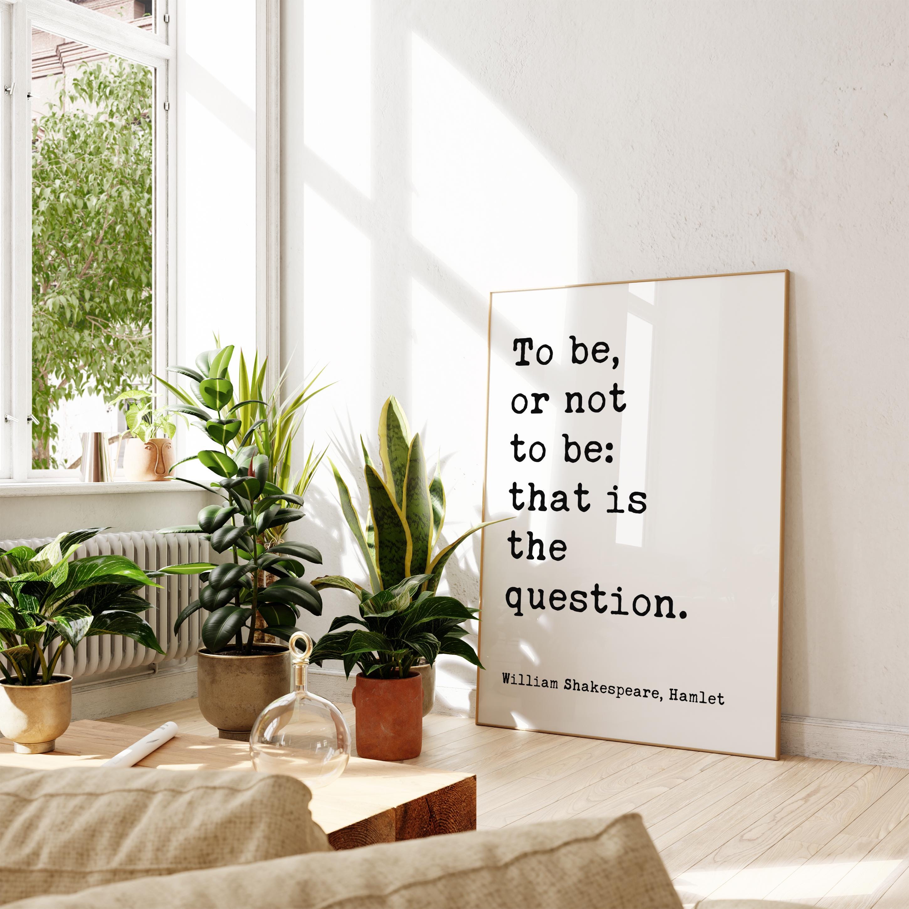 a living room with a large poster on the wall displaying a quote by William Shakespeare, Hamlet, which reads "To be, or not to be: that is the question." The room is decorated with several potted plants, and there is a wooden table with a glass vase on it.