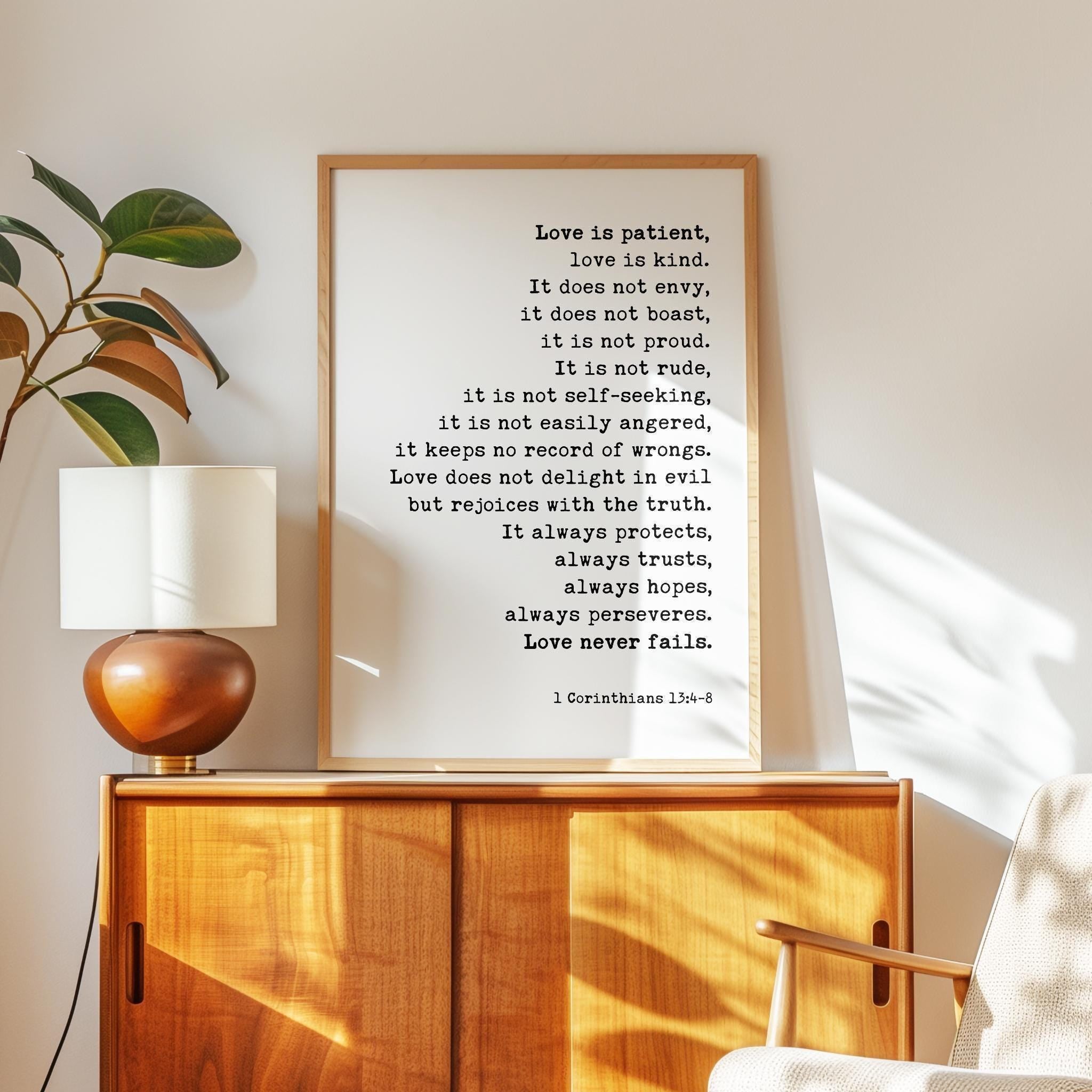 May include: A framed print with the text "Love is patient, love is kind." The print is in a wooden frame and is displayed on a wooden cabinet. A lamp with a white shade and a brown base sits on the cabinet.
