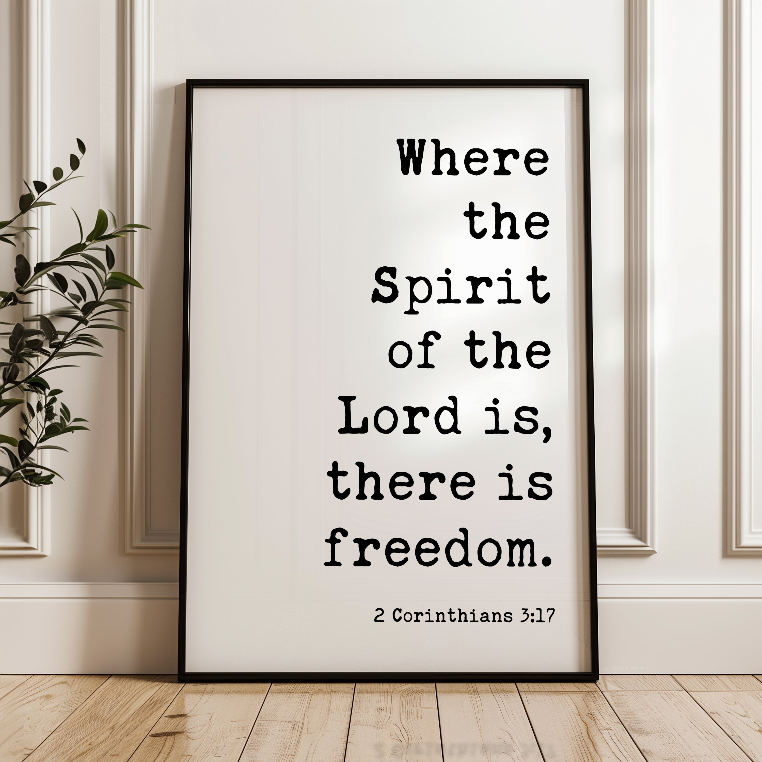 A framed poster with the text "Where the Spirit of the Lord is, there is freedom." and the Bible verse "2 Corinthians 3:17" is displayed on a wooden floor against a white wall.