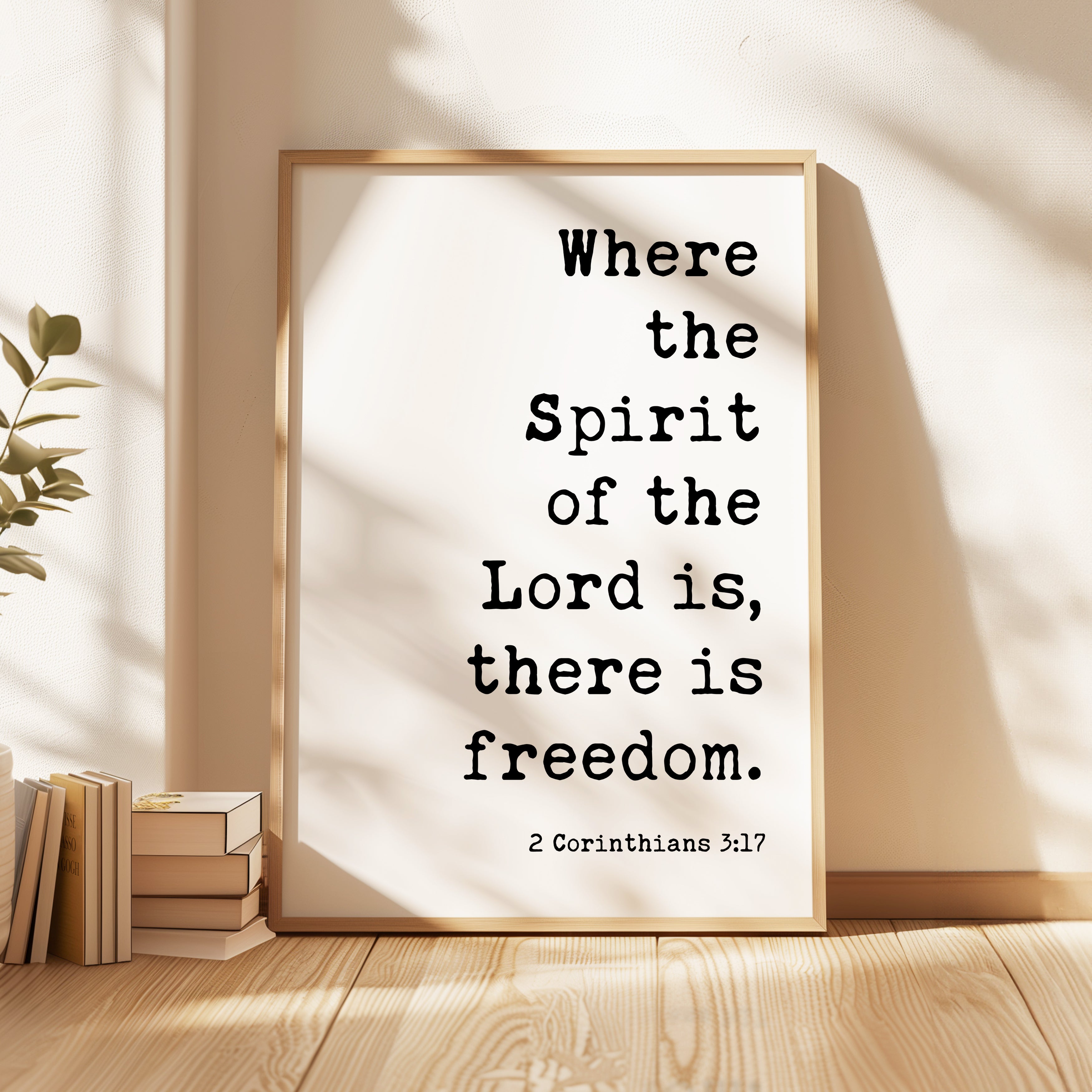 A framed print with the text "Where the Spirit of the Lord is, there is freedom" is displayed on a wooden floor next to a stack of books.