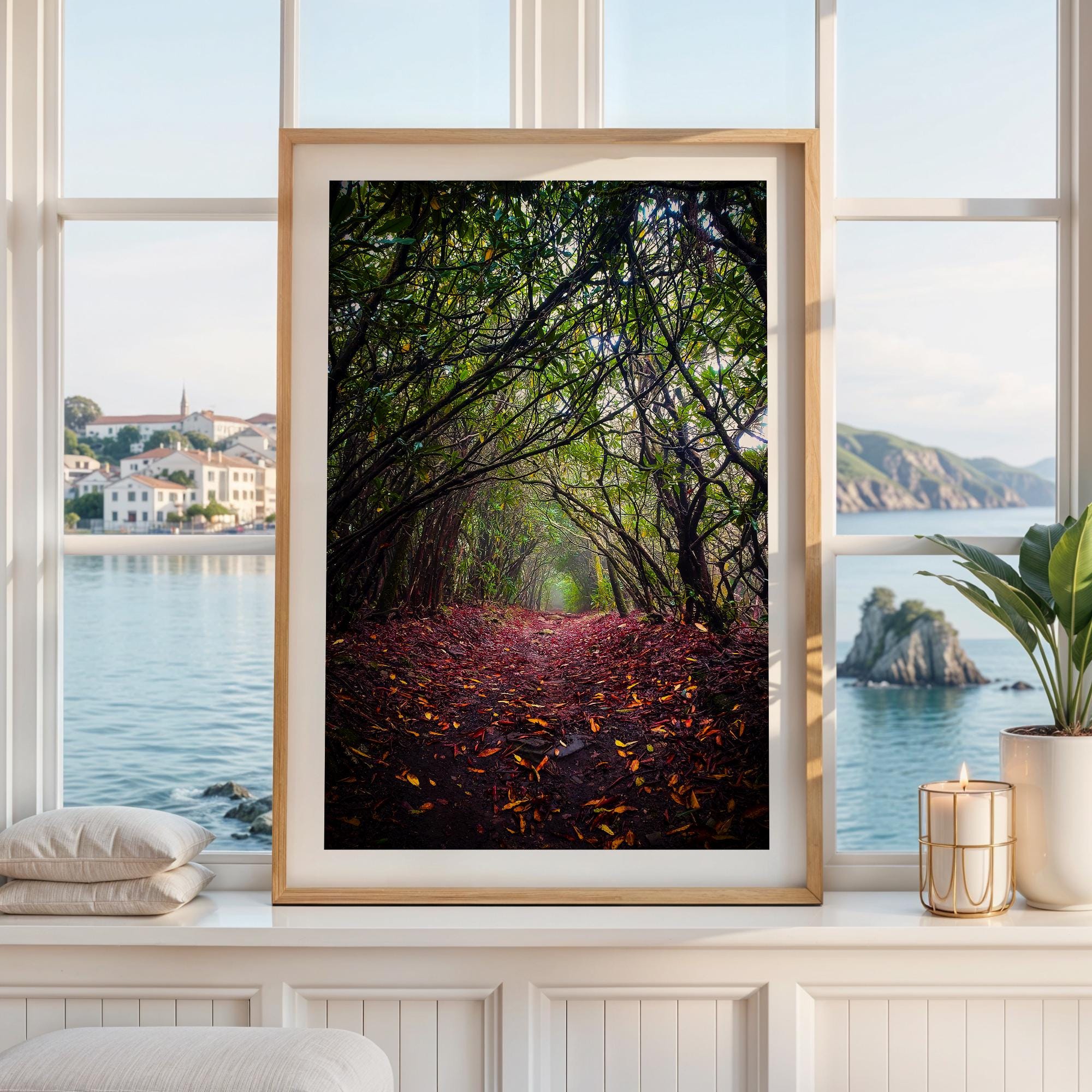 a framed photograph of a forest path with fallen leaves, framed by a window overlooking a scenic view of a body of water and a distant town.