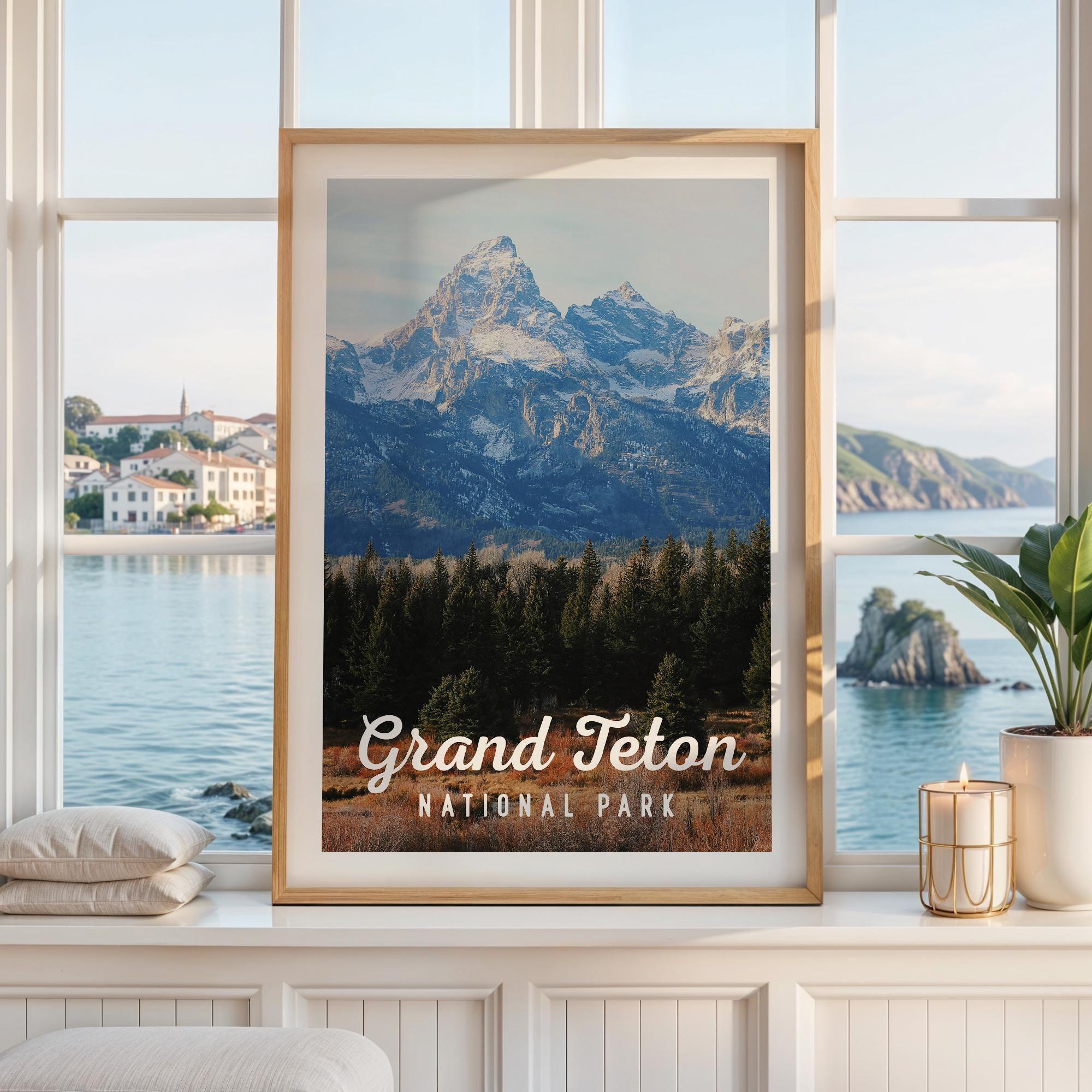 May include: A framed vertical wall art print featuring a landscape of the snow-capped Grand Teton mountains above a dark green pine forest and brown brush, with the white text Grand Teton NATIONAL PARK printed at the bottom of the image.