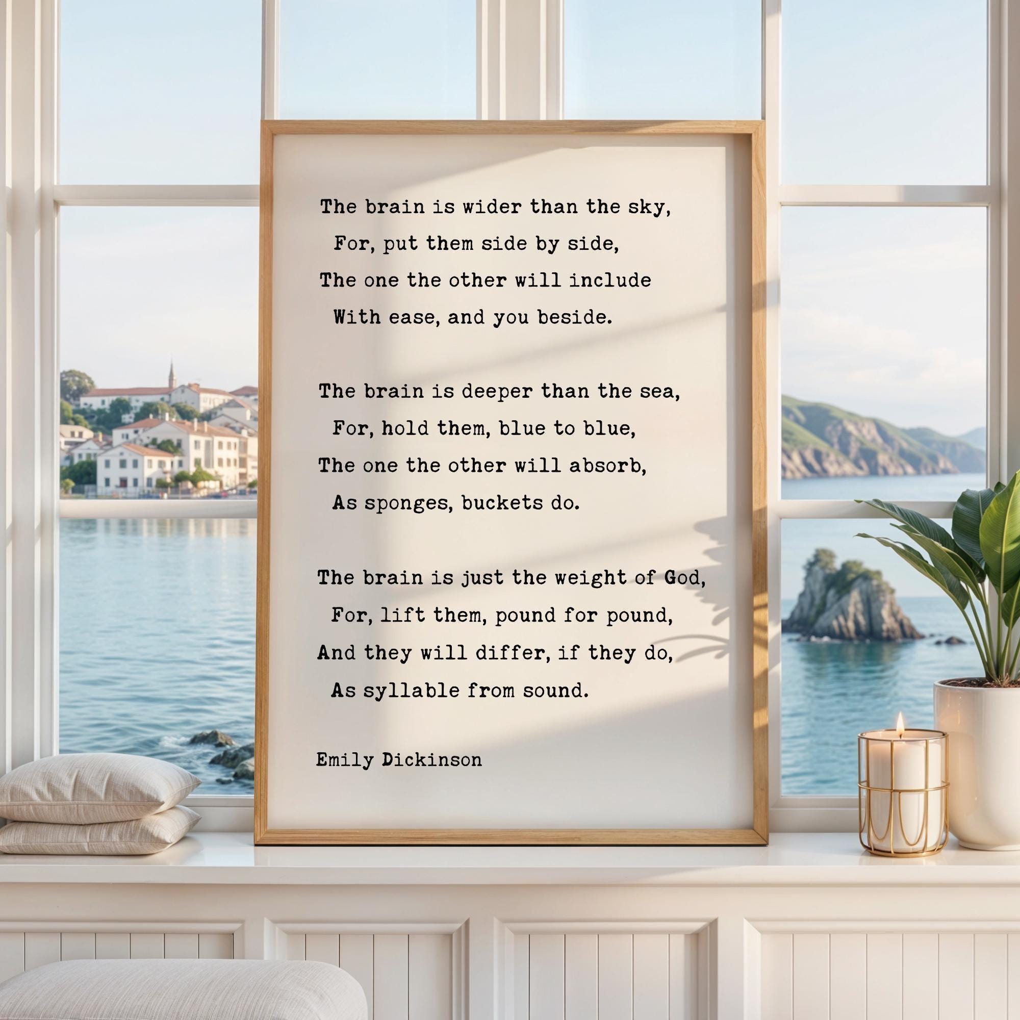 May include: A framed print featuring a poem by Emily Dickinson. The text is in black against a cream-colored background. The frame is a light brown color. The print is displayed on a white windowsill with a view of the ocean.