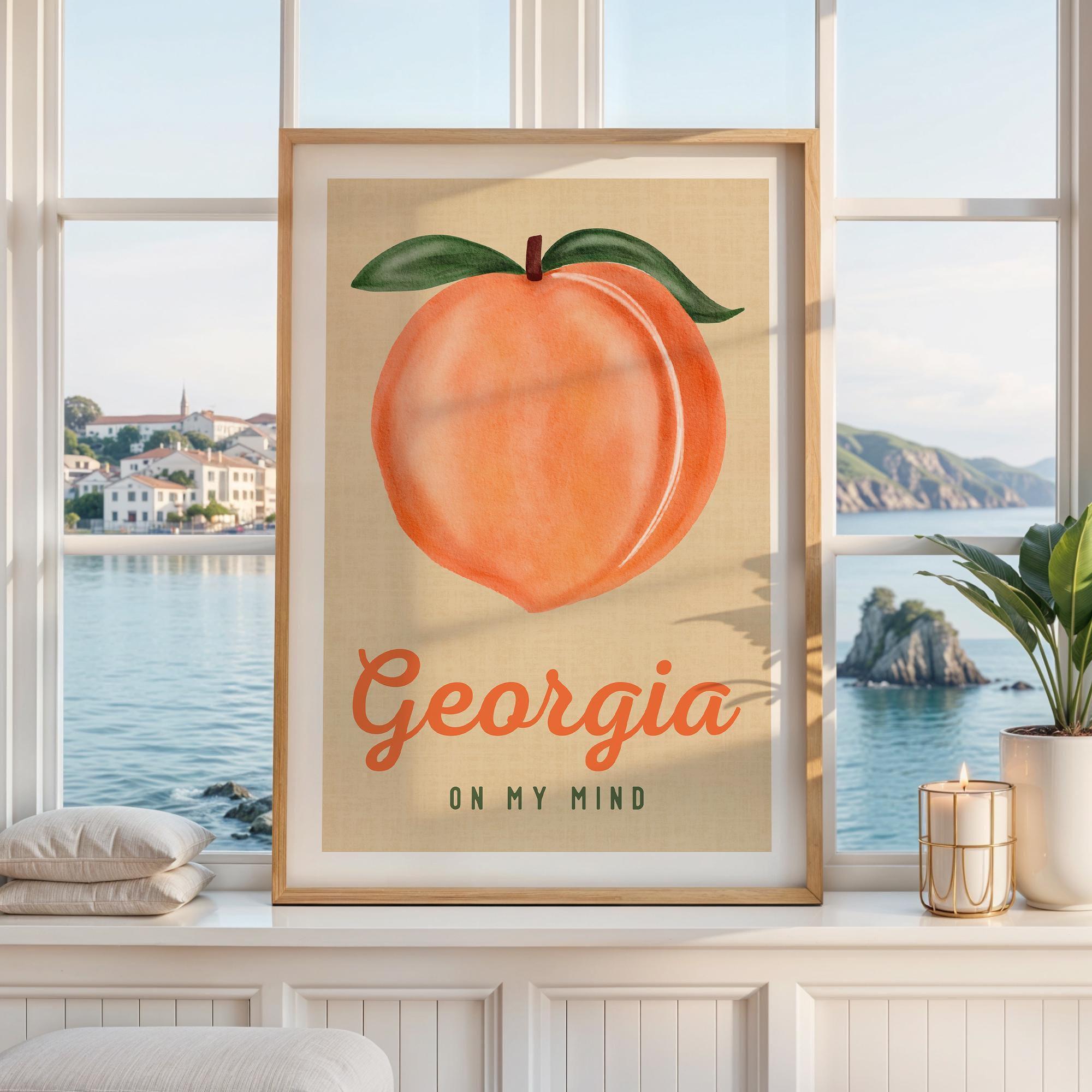 May include: A framed wall art print featuring a large, centered illustration of a peach with green leaves on a light tan background. Below the peach, the text reads Georgia in a large orange script font and ON MY MIND in smaller dark green text.