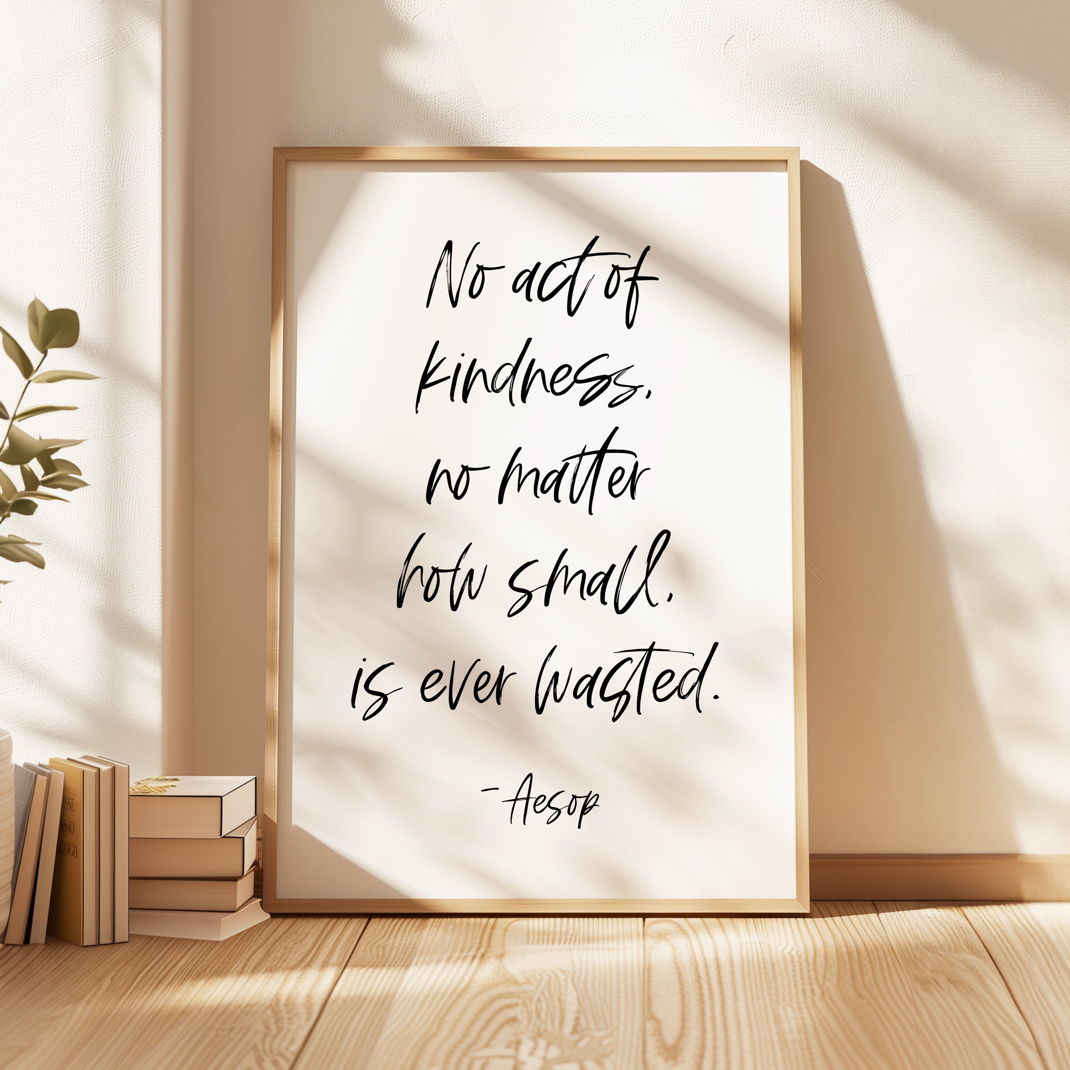 a framed quote by Aesop that reads "No act of kindness, no matter how small, is ever wasted." The quote is displayed on a white background within a wooden frame, and there are some books and a plant visible in the background.