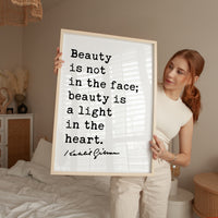 A woman holding a framed poster with a quote about beauty, standing in a bedroom.