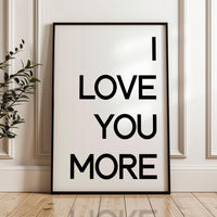 May include: Black framed wall art with a minimalist design. The poster features the text 'I LOVE YOU MORE' in bold, uppercase, black lettering on a white background.  The simple typography creates a modern and romantic feel, suitable for home decor or as a gift. The poster's clean aesthetic makes it a versatile piece for various interior styles.