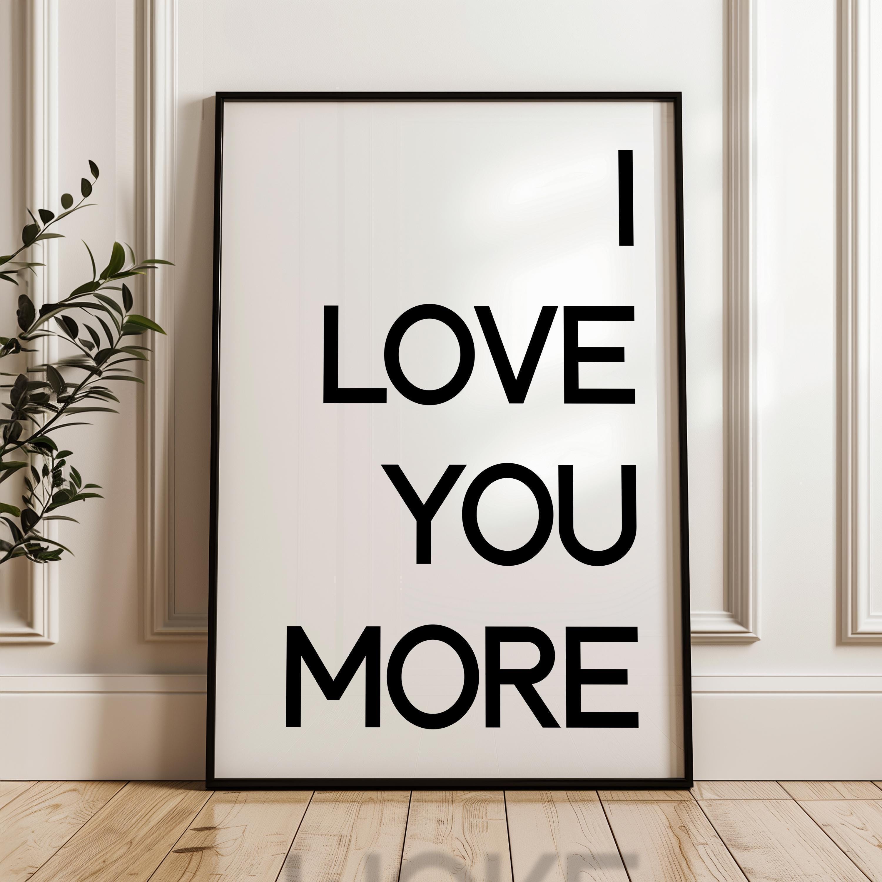 May include: Black framed wall art with a minimalist design. The poster features the text 'I LOVE YOU MORE' in bold, uppercase, black lettering on a white background.  The simple typography creates a modern and romantic feel, suitable for home decor or as a gift. The poster's clean aesthetic makes it a versatile piece for various interior styles.