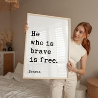A woman holding a framed poster with the text "He who is brave is free" by Seneca.