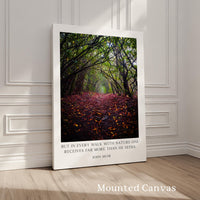 A framed photograph of a forest path covered in fallen leaves, with a quote by John Muir superimposed on the image.