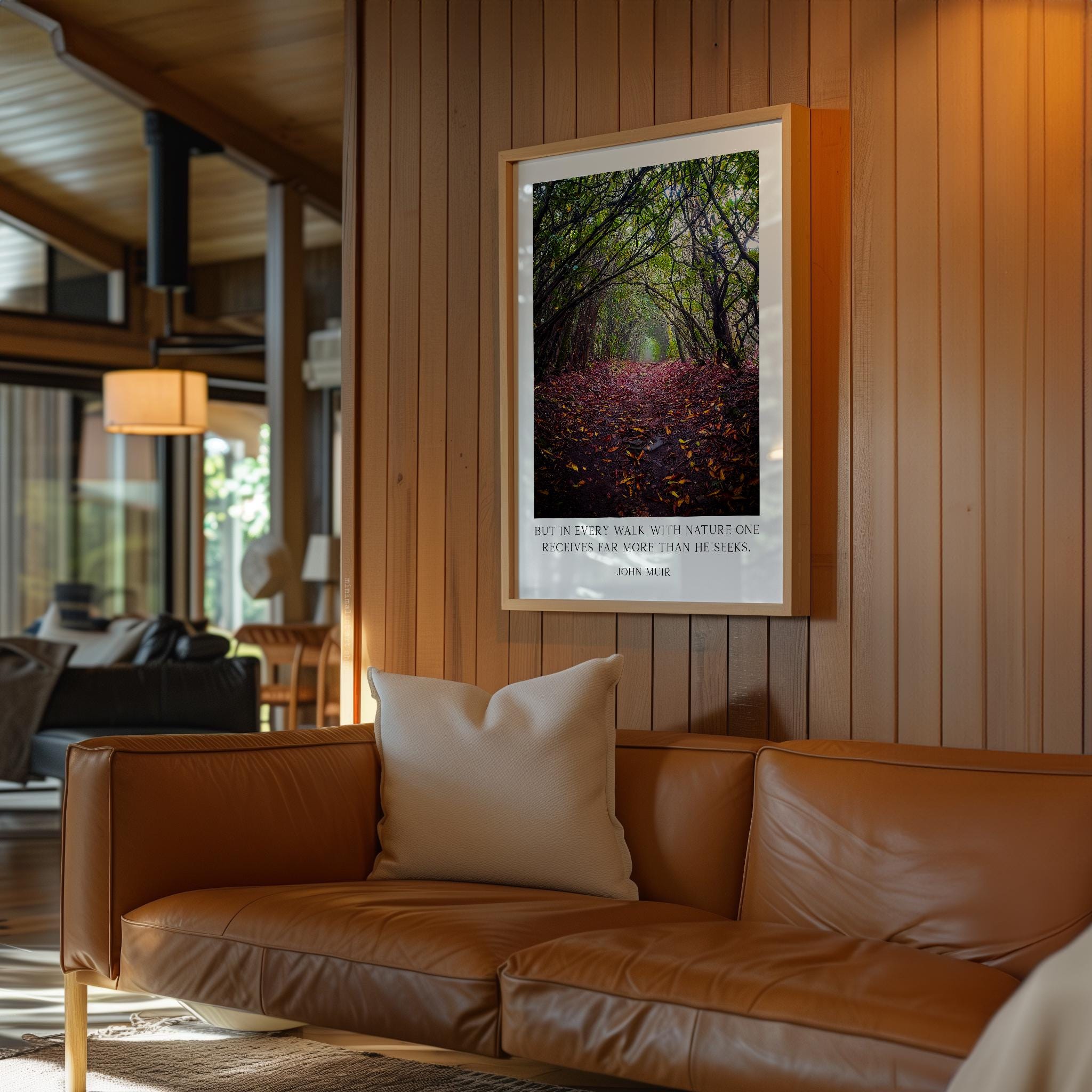 a cozy living room with a brown leather sofa, a framed photograph of a forest path with red leaves, and a wooden wall.