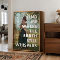 May include: A framed art print featuring a vintage-style painting of a woman in a garden, with the text "FIND ME WHERE THE EARTH STILL WHISPERS" in white. The artwork is in a wooden frame, displayed in a well-lit room.