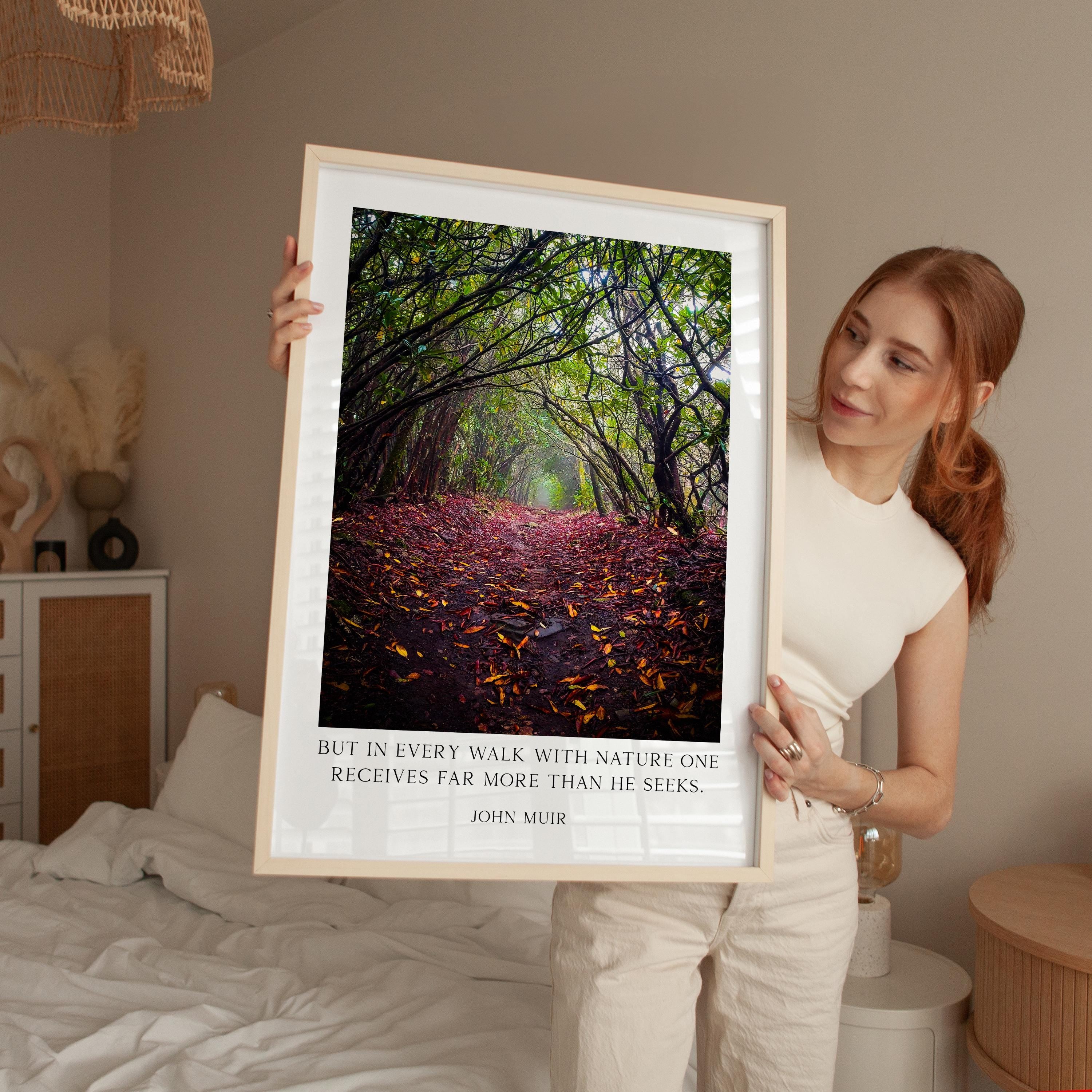 A woman holds up a framed photograph of a forest path with fallen leaves, accompanied by a quote about nature and the value of every walk.