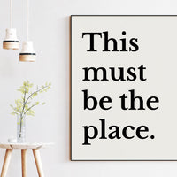 a minimalist interior design with a framed quote, a small table with a vase of flowers, and two hanging light fixtures.