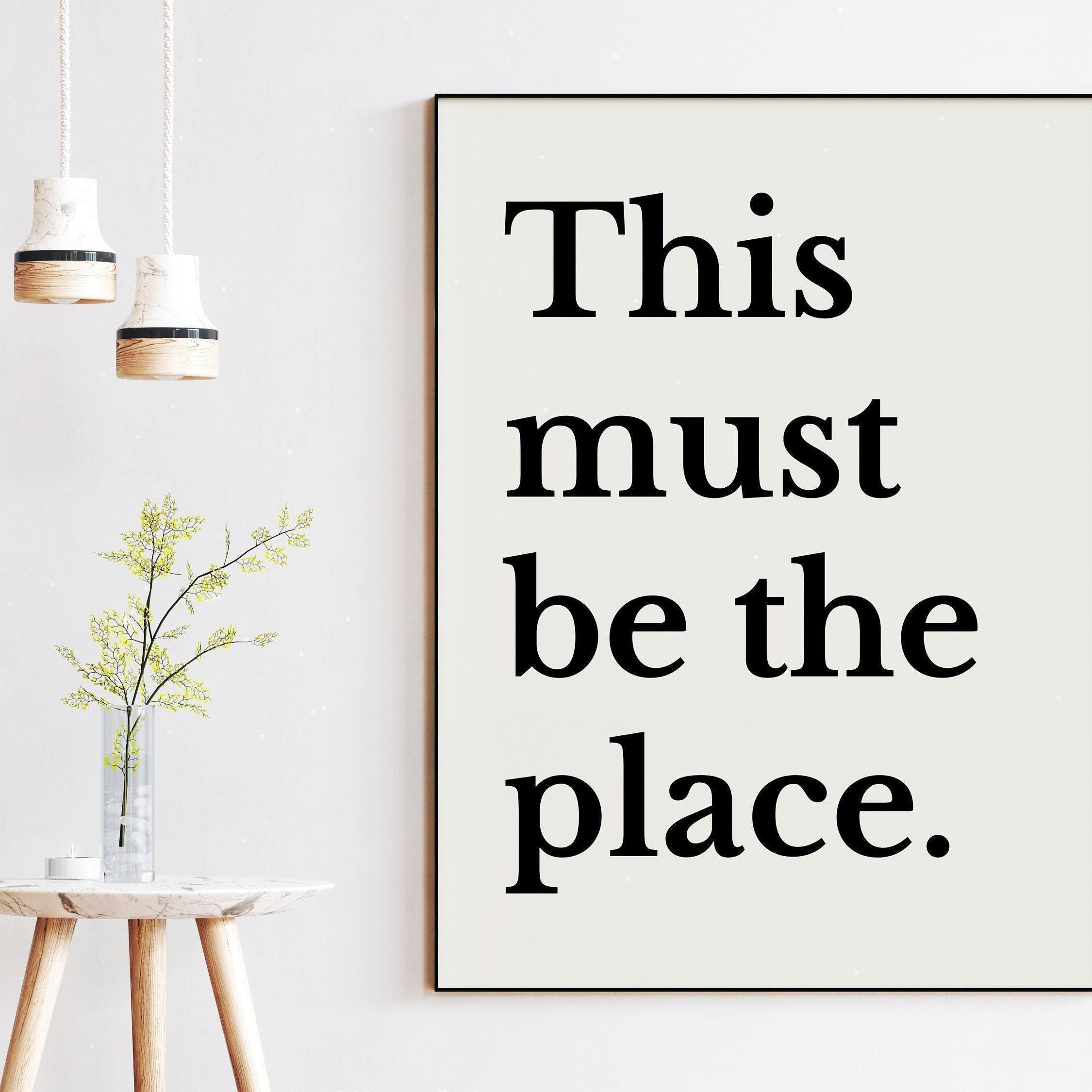 a minimalist interior design with a framed quote, a small table with a vase of flowers, and two hanging light fixtures.