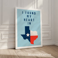 A framed poster with the text "I FOUND MY HEART IN" and a graphic of the state of Texas, standing on a wooden floor against a white wall.