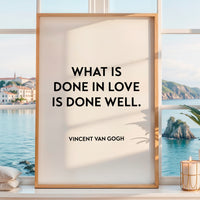 a framed quote by Vincent Van Gogh, "What is done in love is done well." The quote is displayed in a white frame with a wooden border, and it is set against a scenic view of a body of water and a coastal town.