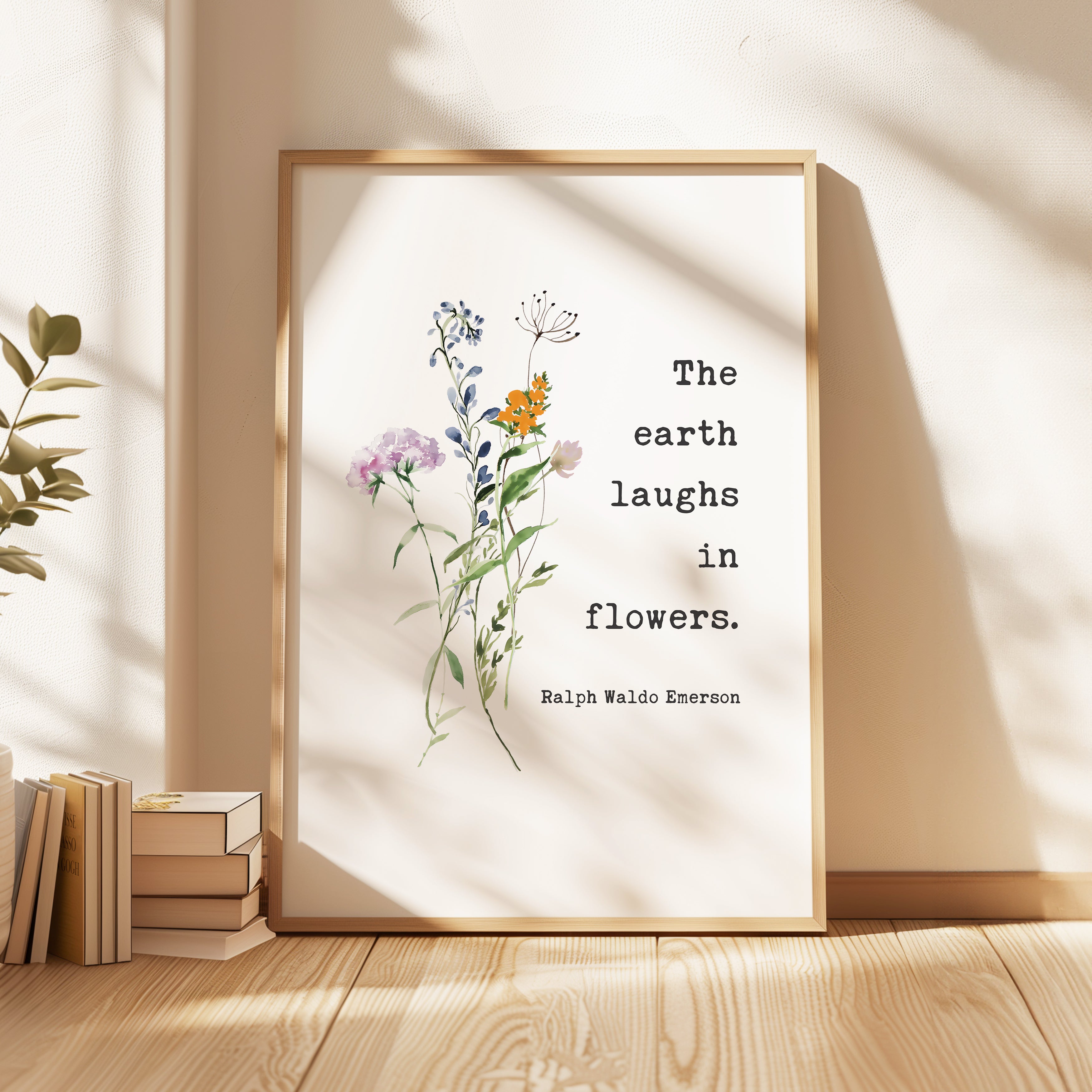 a framed quote by Ralph Waldo Emerson, "The earth laughs in flowers," which is displayed on a wooden surface next to a stack of books.