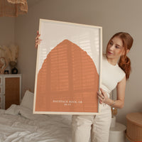 A woman holding a framed print of a large orange shape in a bedroom.