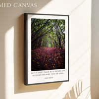A framed canvas hanging on a wall, depicting a forest path with fallen leaves and a quote by John Muir about the beauty of nature.