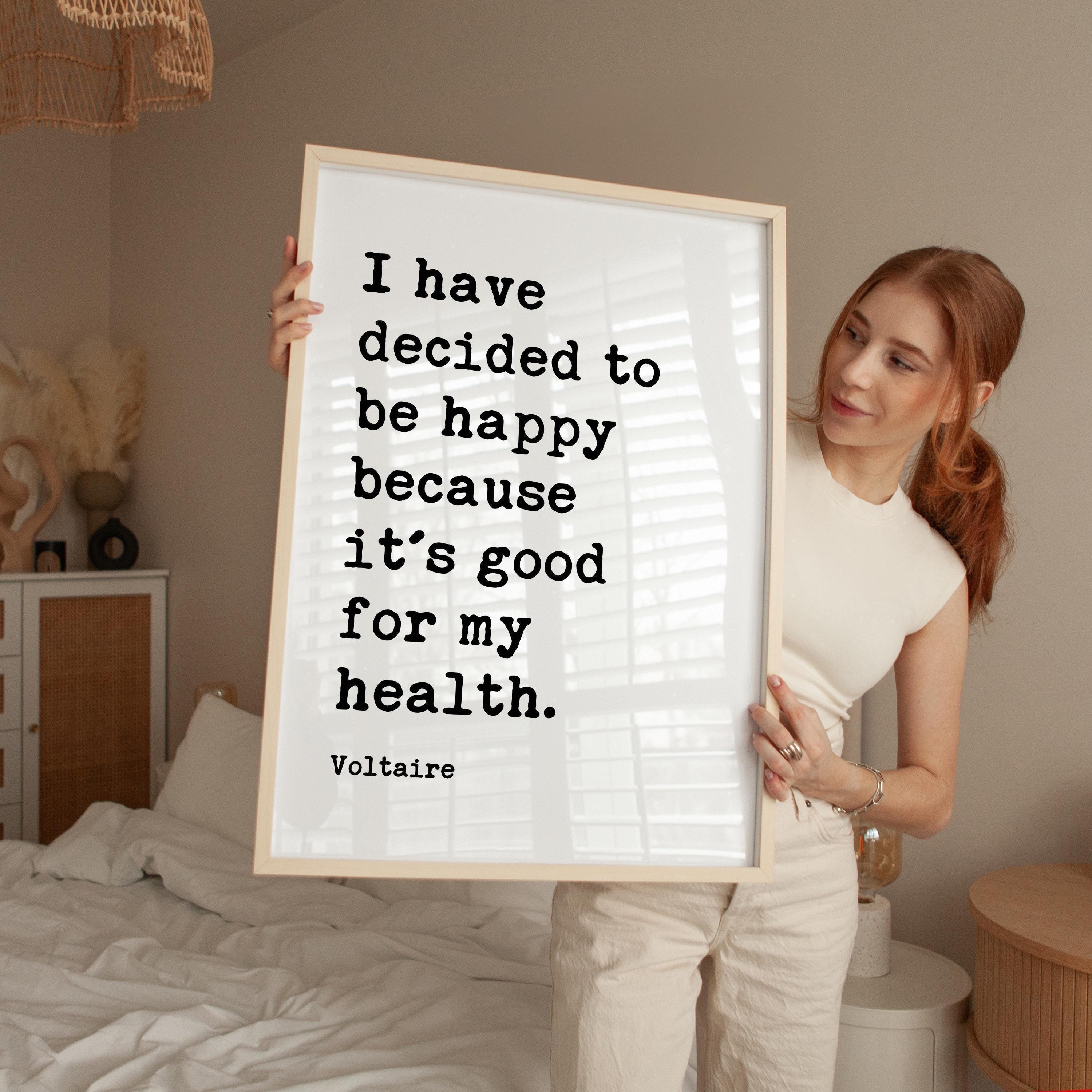 A woman holding a framed poster with a quote on it, standing in a bedroom.