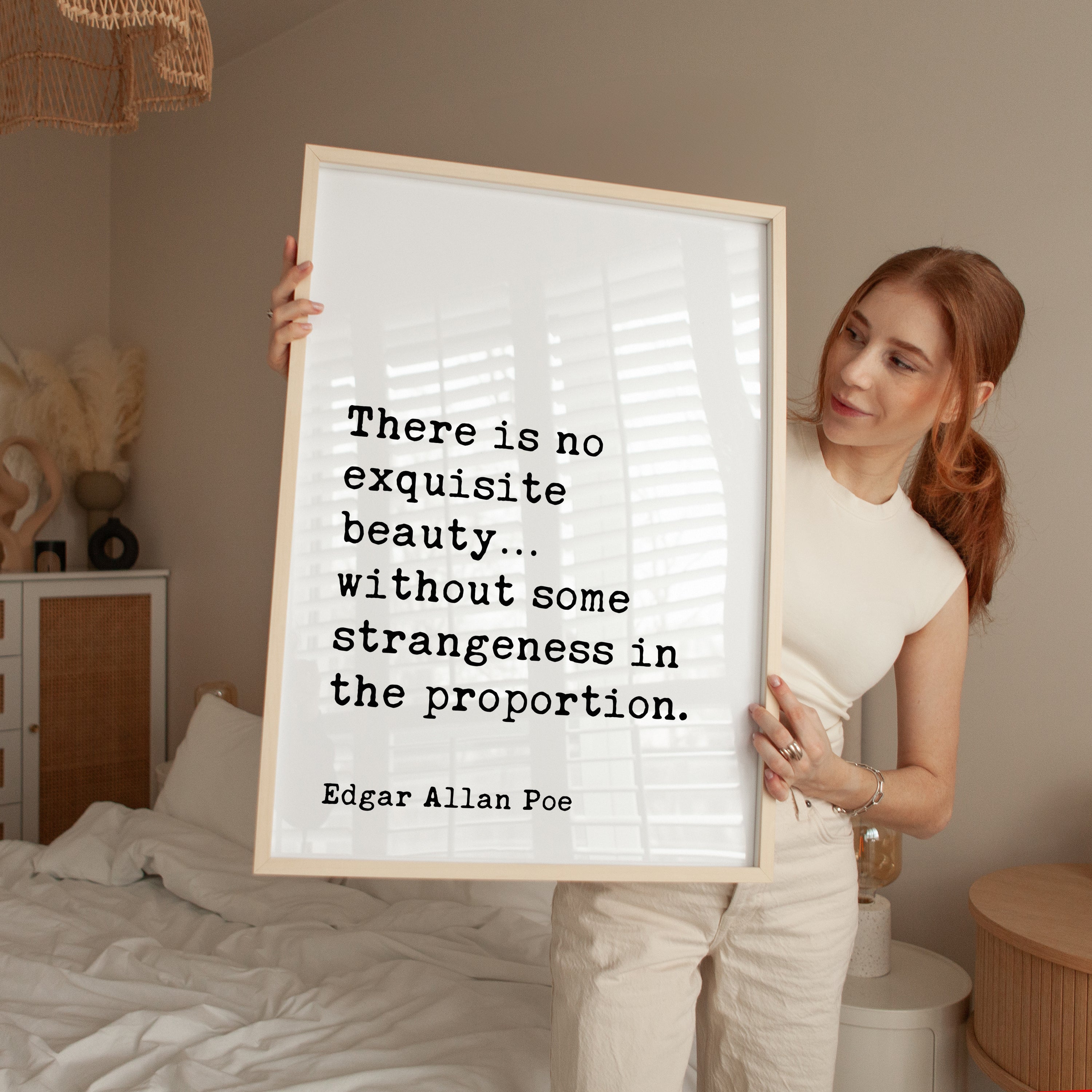 A woman holding a framed quote by Edgar Allan Poe in a bedroom setting.